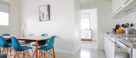 A modern kitchen with white cabinets, a stainless steel sink, and a dining area with a wooden table and blue chairs.