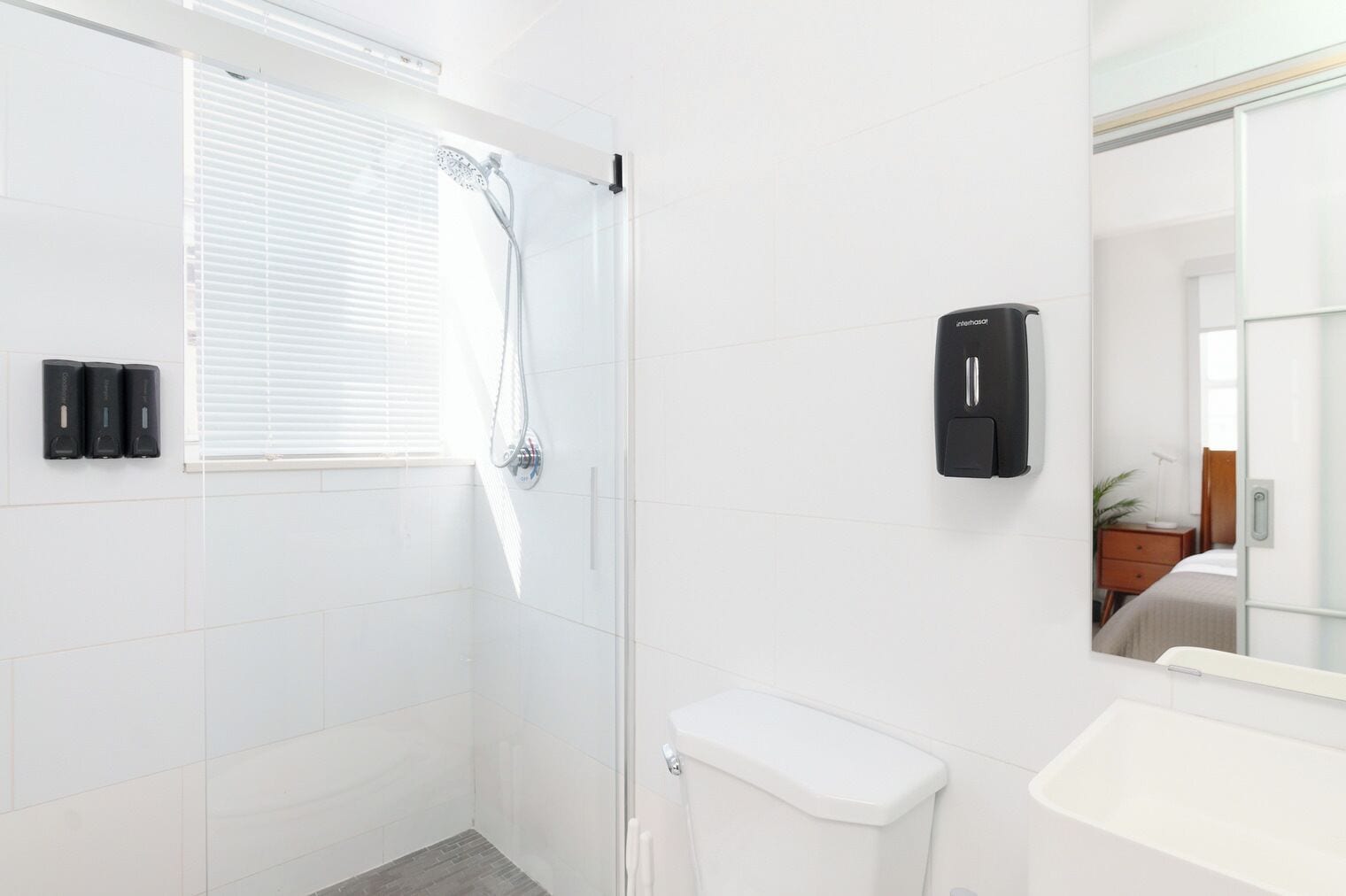 A modern bathroom with a glass shower enclosure, a toilet, a sink, and a hand dryer.