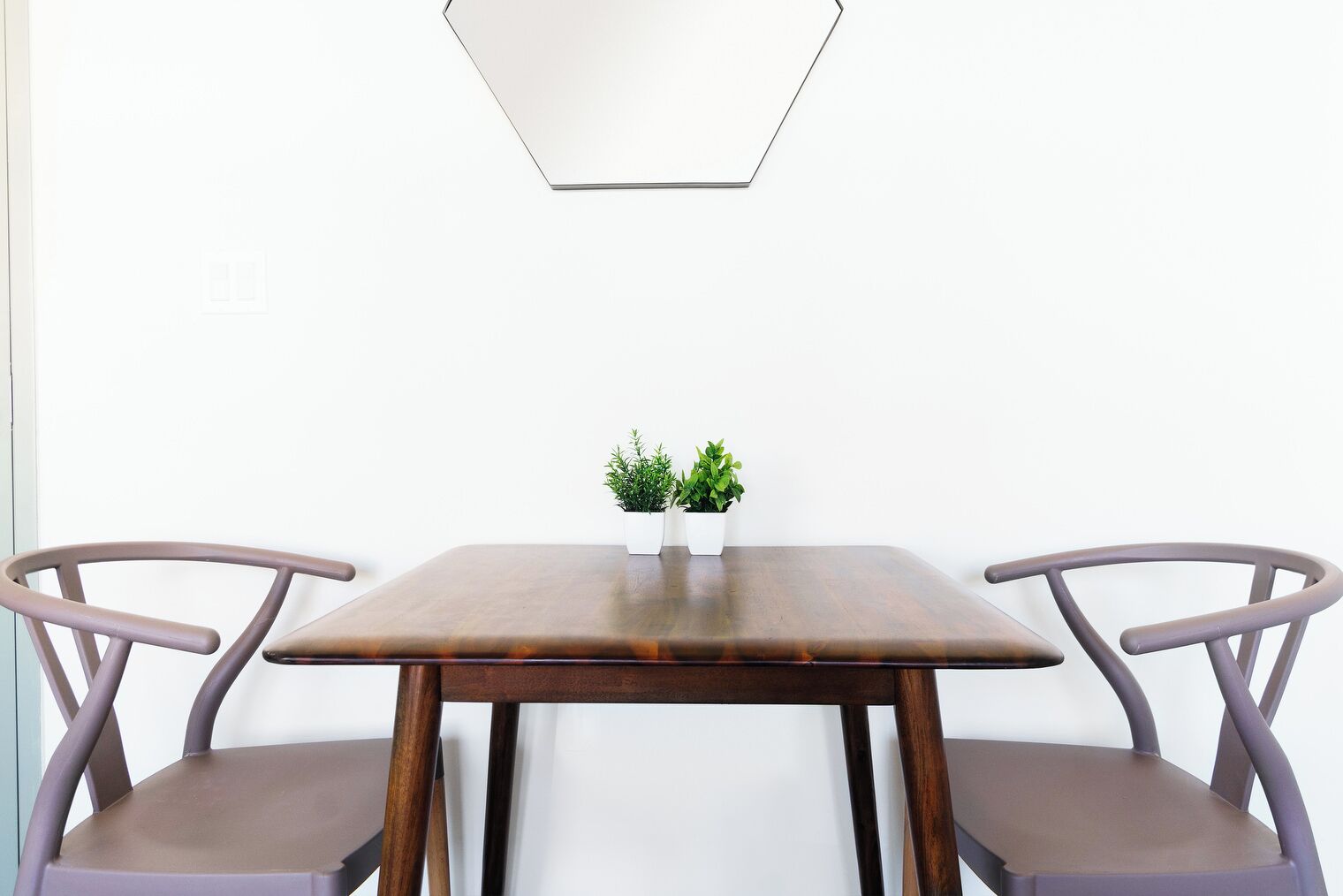 Et spisebord med to stole, en lille potteplante og en geometrisk lampe på væggen.