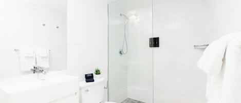 A modern bathroom with a glass-enclosed shower, a white toilet, and a vanity with a mirror and sink.