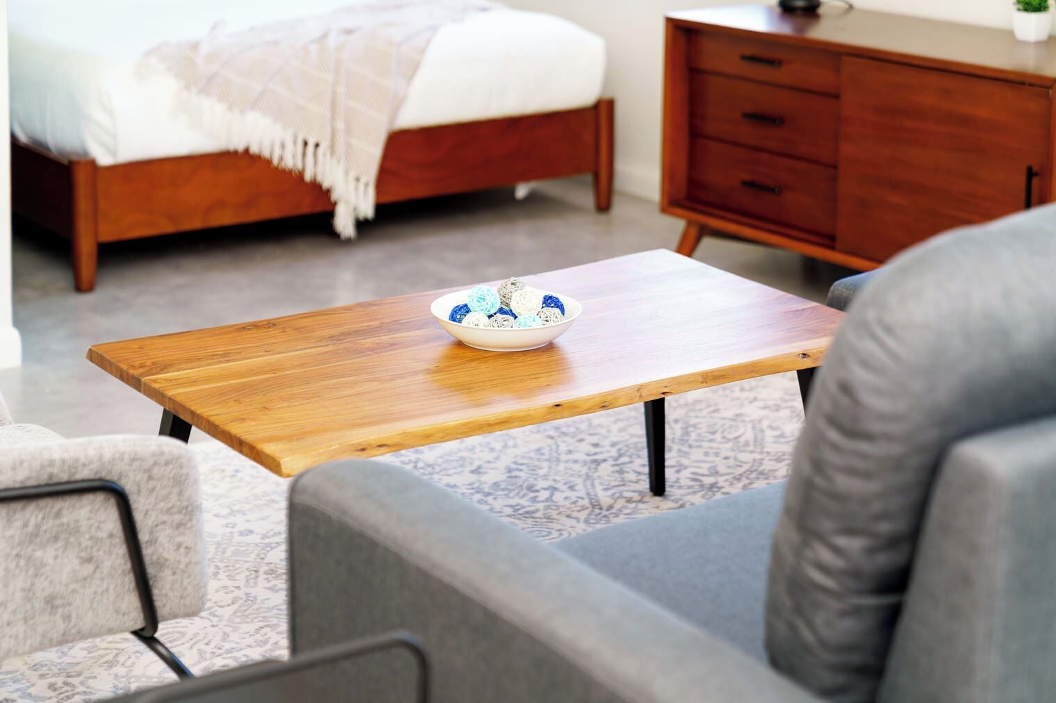 A modern living room with a wooden coffee table, a bowl of decorative items, a grey sofa, and a wooden cabinet.