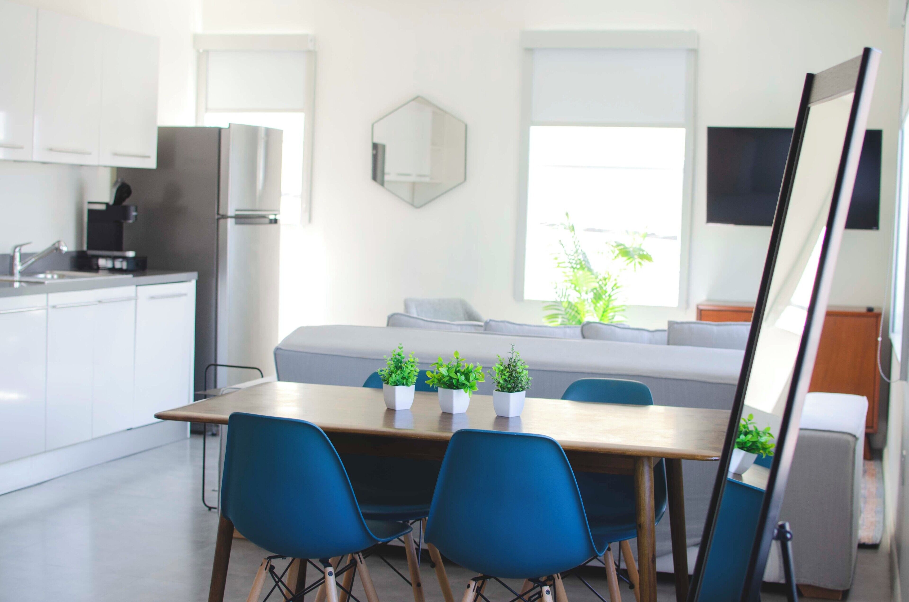 A modern kitchen with white cabinets, a stainless steel refrigerator, and a dining area with a wooden table and blue chairs.