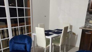 Un coin repas avec une table et des chaises blanches, un canapé bleu et un balcon avec vue.