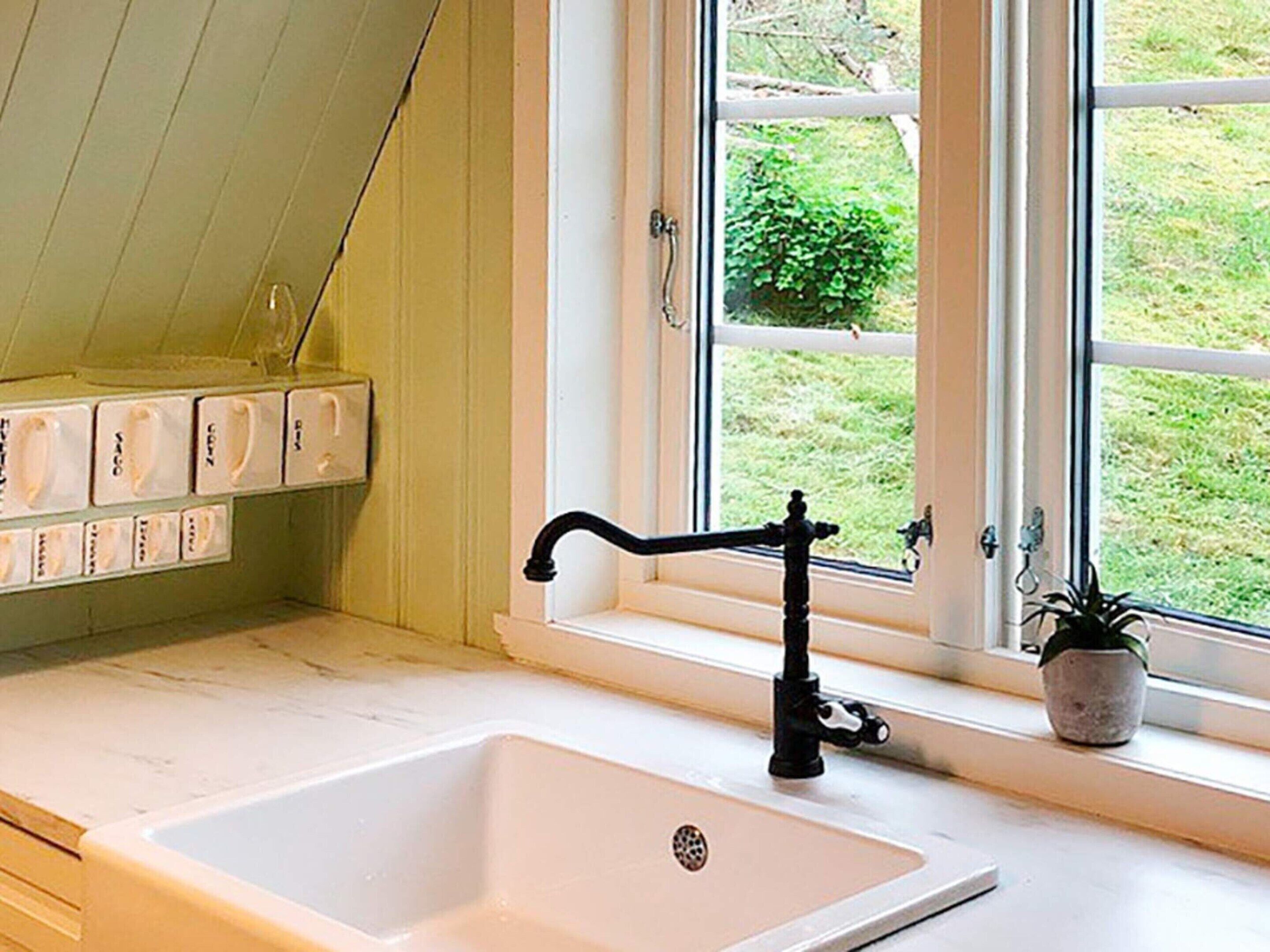 Ein Badezimmer mit einem weißen Waschbecken, einem schwarzen Wasserhahn und einem Fenster mit Blick auf Grünflächen.