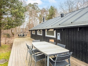 A wooden deck with a table and chairs, a covered outdoor area, and a building with a metal roof. - 6 Person Holiday Home in Knebel (Knebel)