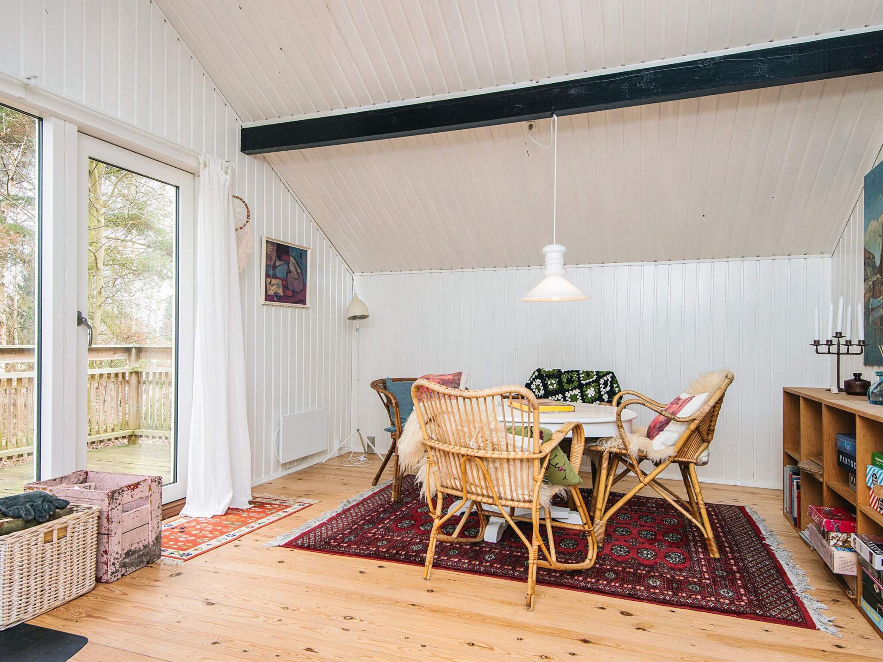 Una habitación acogedora con suelo de madera, sillas de mimbre, una mesa y un tapete rojo estampado.