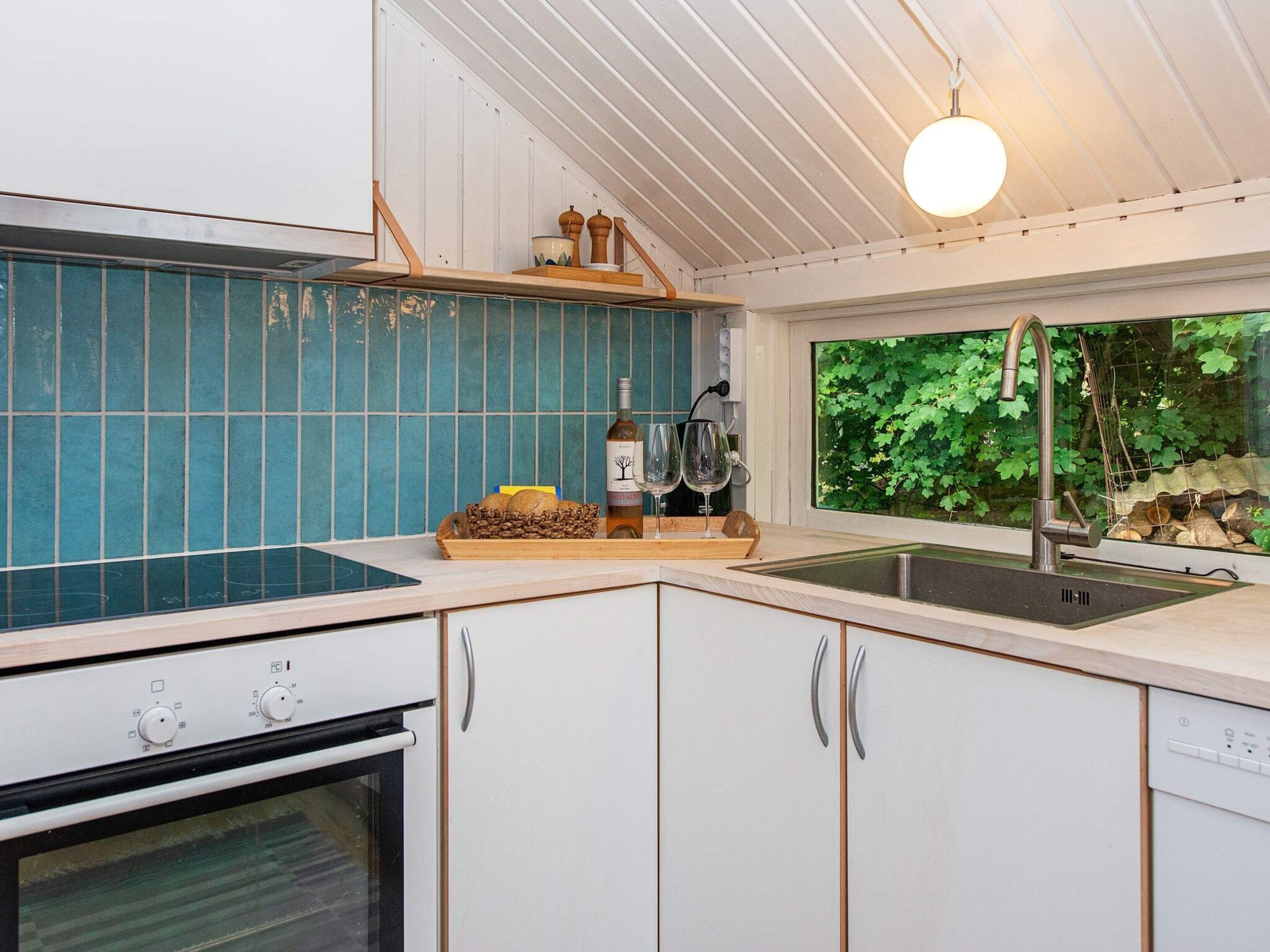A modern kitchen with a built-in oven, a sink, and a window with a view of greenery.