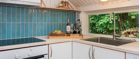 A modern kitchen with a built-in oven, a sink, and a window with a view of greenery.