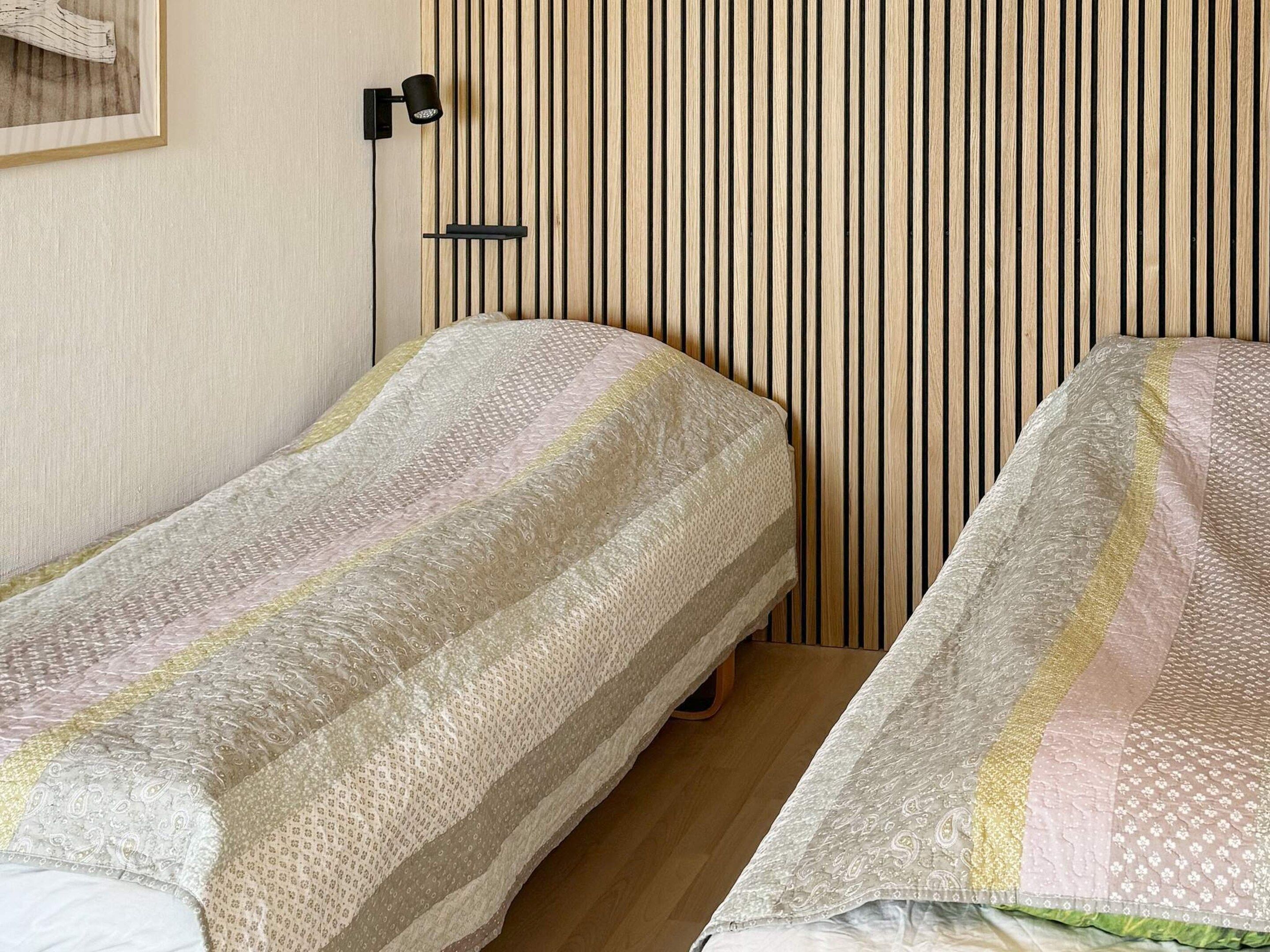 A room with two single beds, a wall-mounted light fixture, and a wooden slat wall design.