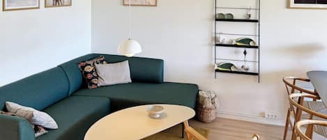 A modern living room with a teal sofa, a small round table, and a wicker chair.