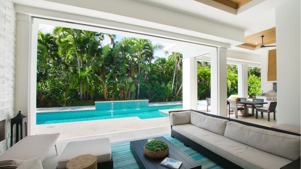 A modern living room with a large glass door leading to a swimming pool surrounded by lush greenery. - Luxury Modern Newly Built House in Naples (Naples)