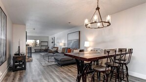 Ein geräumiges Wohnzimmer mit Essbereich, ausgestattet mit einem Holztisch und Stühlen, einer Couch und einer Pendelleuchte.