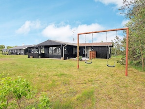 A black building with a porch and a swing set in a grassy field. - 5 Person Holiday Home in Saeby (Sæby)