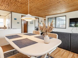 A modern interior with a dining area featuring a table with placemats, a vase with dried plants, and a sofa. - 5 Person Holiday Home in Saeby (Sæby)