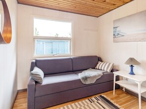 A room with a grey sofa, a white side table with a lamp, a window with blinds, and a painting on the wall. - 5 Person Holiday Home in Saeby (Sæby)