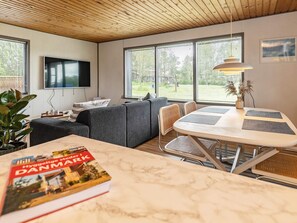 A modern living room with a sofa, a dining table, and a TV mounted on the wall. - 5 Person Holiday Home in Saeby (Sæby)