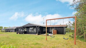 A black building with a porch and a swing set in a grassy field. - 5 Person Holiday Home in Saeby (Sæby)