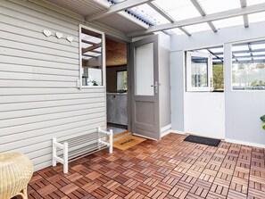 A covered porch with a wooden floor, a white bench, and a door leading to a kitchen area. - 5 Person Holiday Home in Saeby (Sæby)