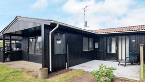 A black wooden house with a covered patio, a satellite dish, and a garden area. - 5 Person Holiday Home in Saeby (Sæby)