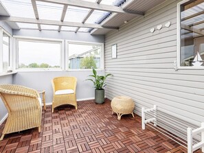 Une terrasse couverte, aménagée avec des meubles en osier, une plante en pot et un sol orné d’un motif en chevrons.