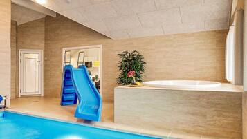 Een binnenzwembad met een blauwe glijbaan, een jacuzzi en een potplant.