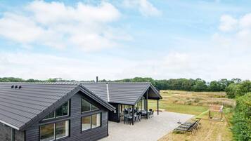 Een modern gebouw met een plat dak en grote ramen, een overdekt terras en uitzicht op een natuurlandschap.
