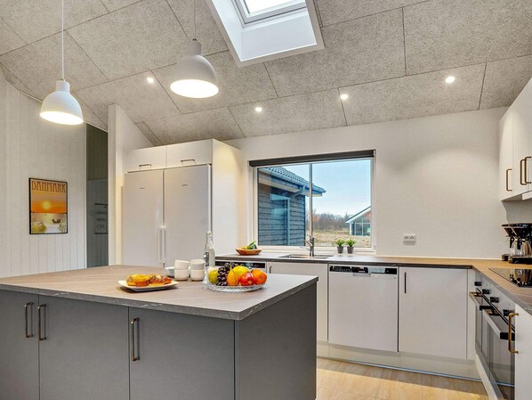 Une cuisine moderne dotée d’un îlot central, de meubles blancs et d’une verrière.