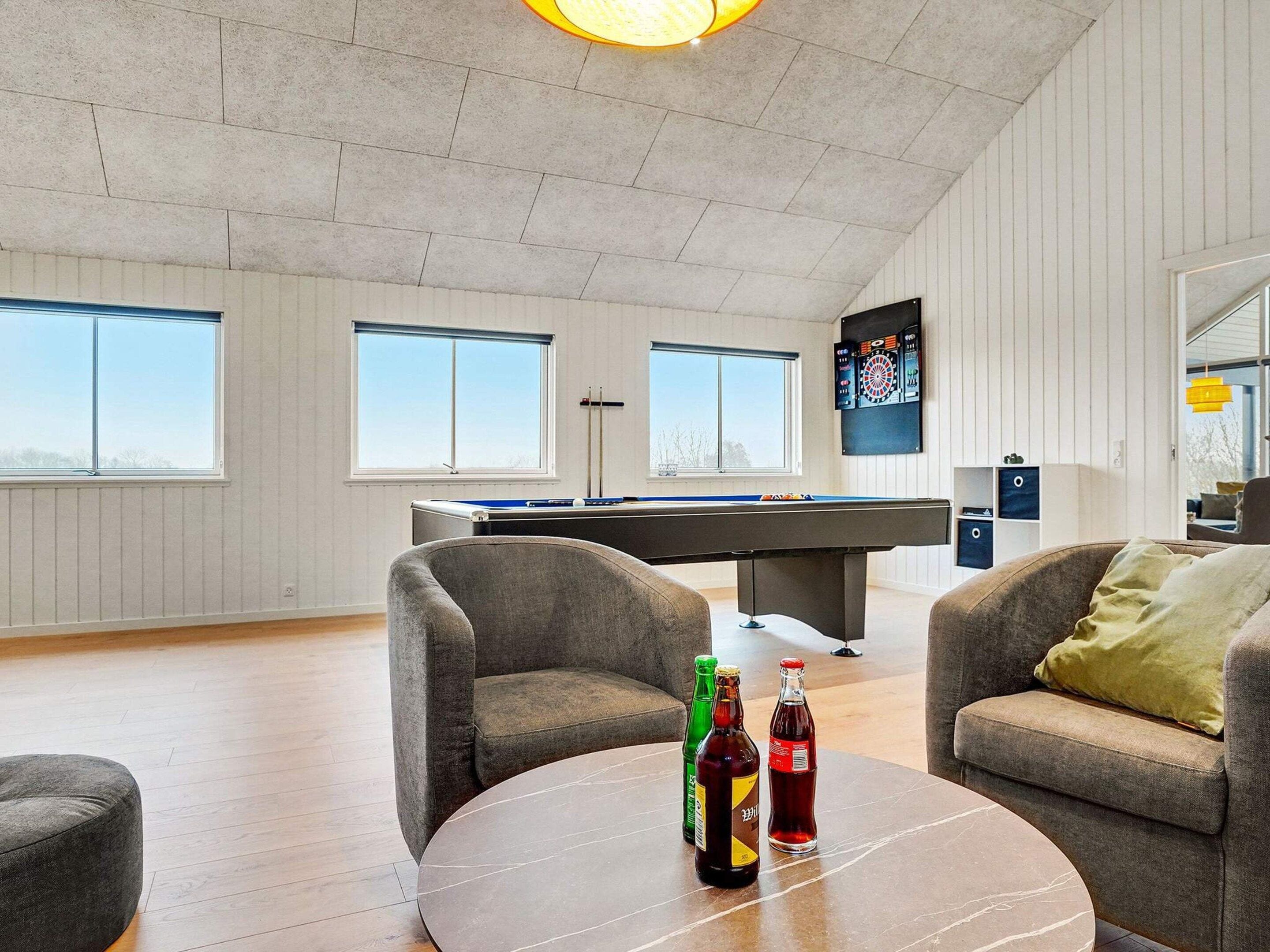 A modern indoor space with a pool table, two armchairs, and a dartboard.