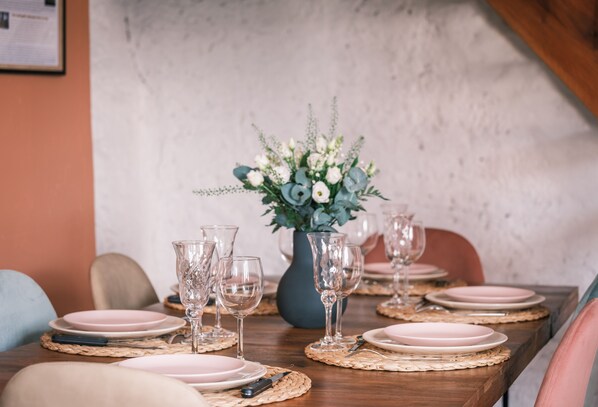 Une table à manger dressée avec des assiettes roses, de la vaisselle transparente et un vase rempli de fleurs.