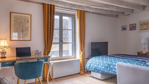 A bedroom with a bed, a desk, a chair, a window with curtains, and a television.