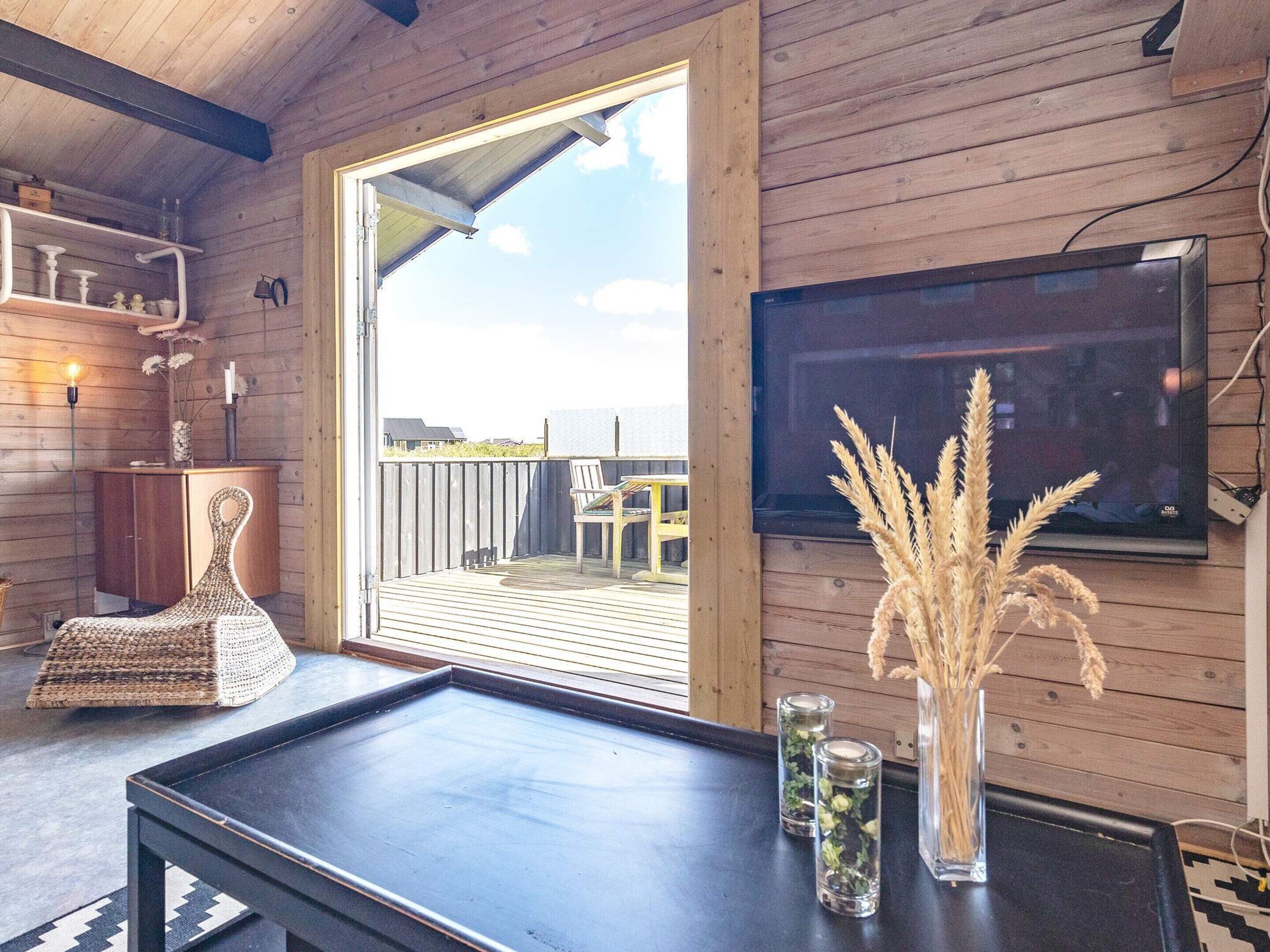 Interior de madera con una televisión, una silla de mimbre, una mesa y vistas al exterior.