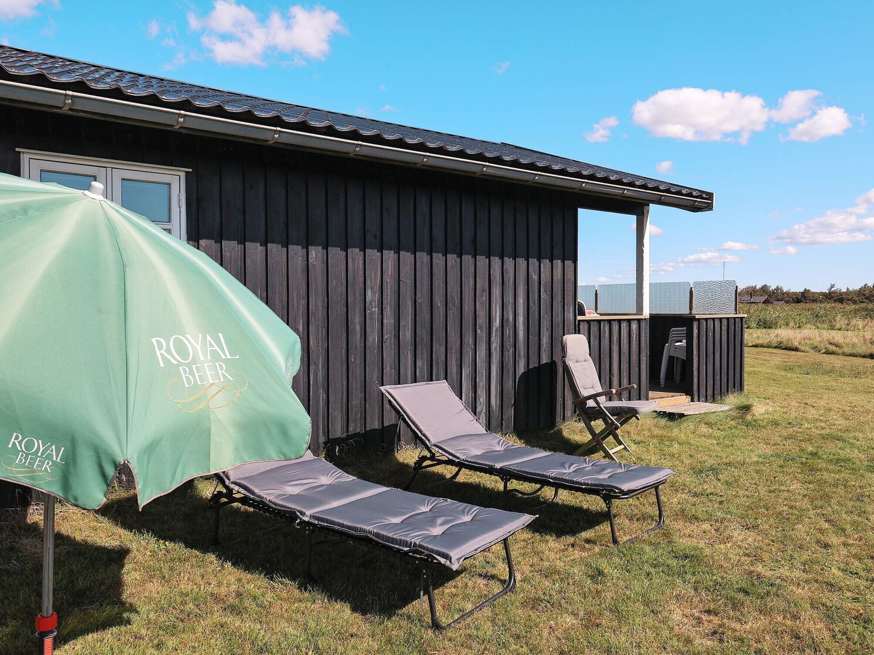 A wooden building with a covered outdoor seating area, including lounge chairs and a table.