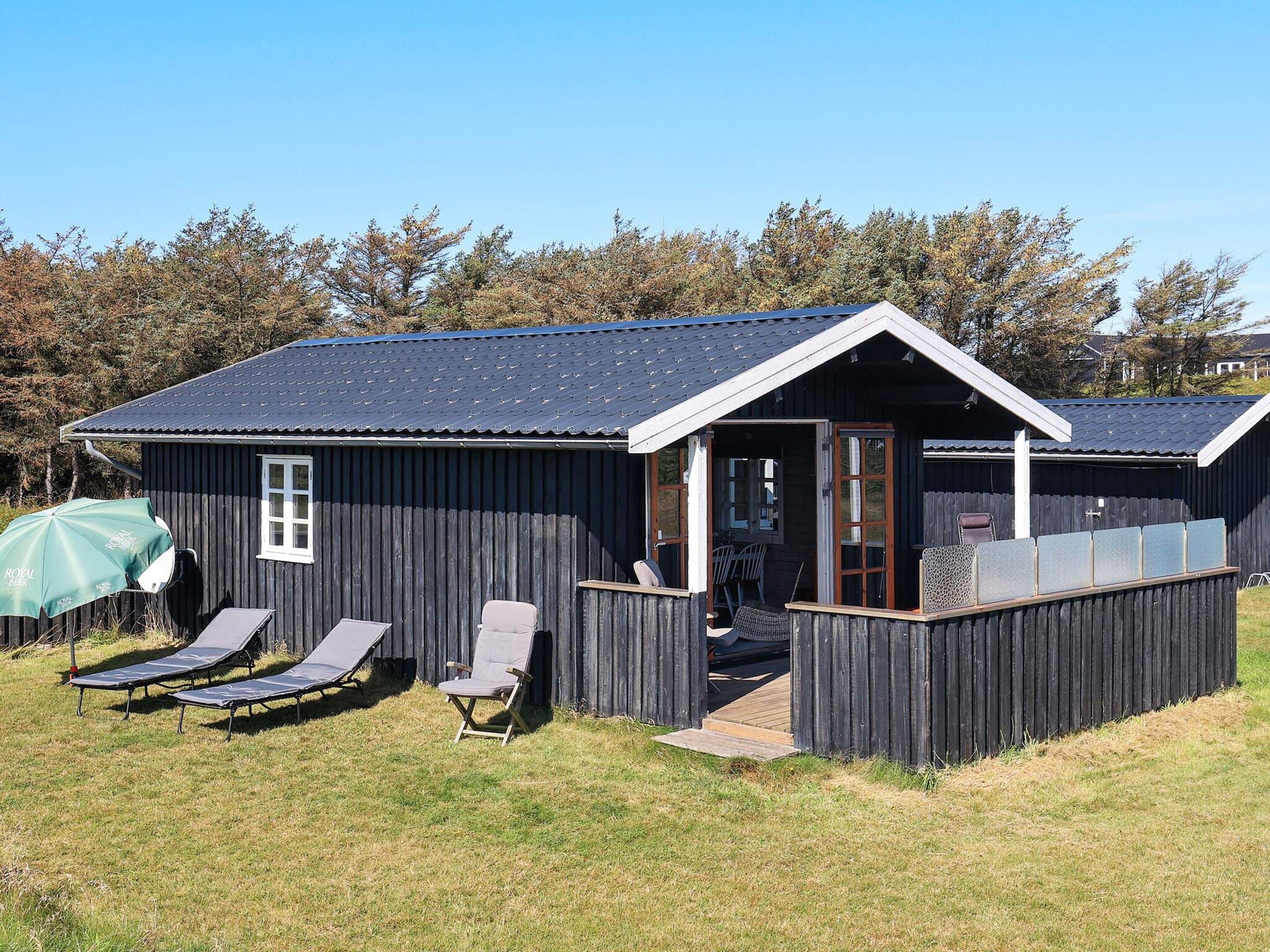 A wooden cabin with a porch, two lounge chairs, and a covered seating area.