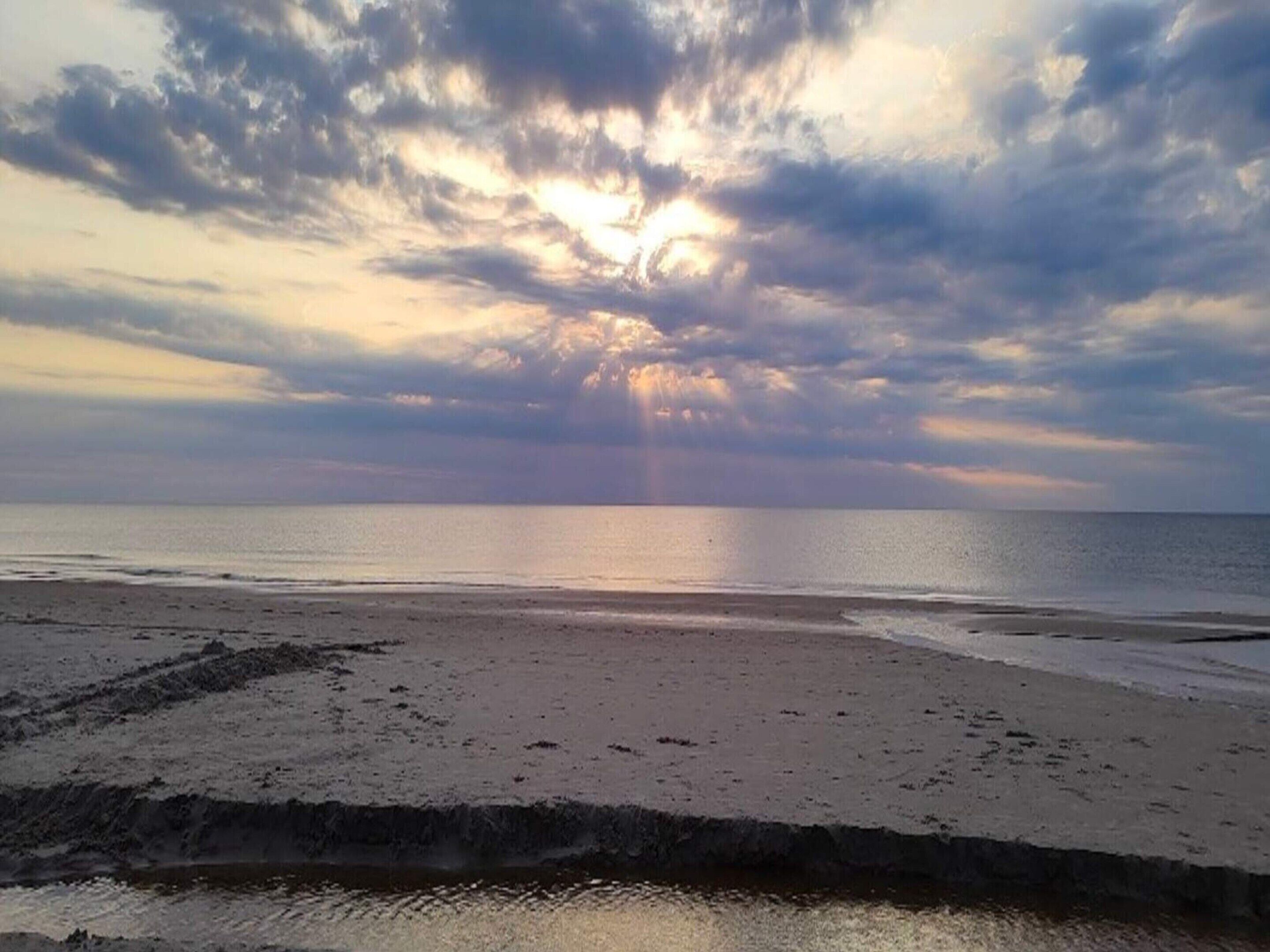 A beach with a cloudy sky and sunlight breaking through.