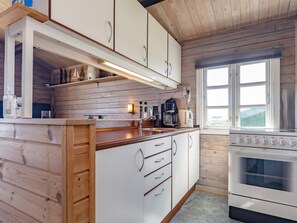 A kitchen with wooden cabinets, a countertop, a stove, and a window. - 4 Person Holiday Home in Lokken (Lokken)