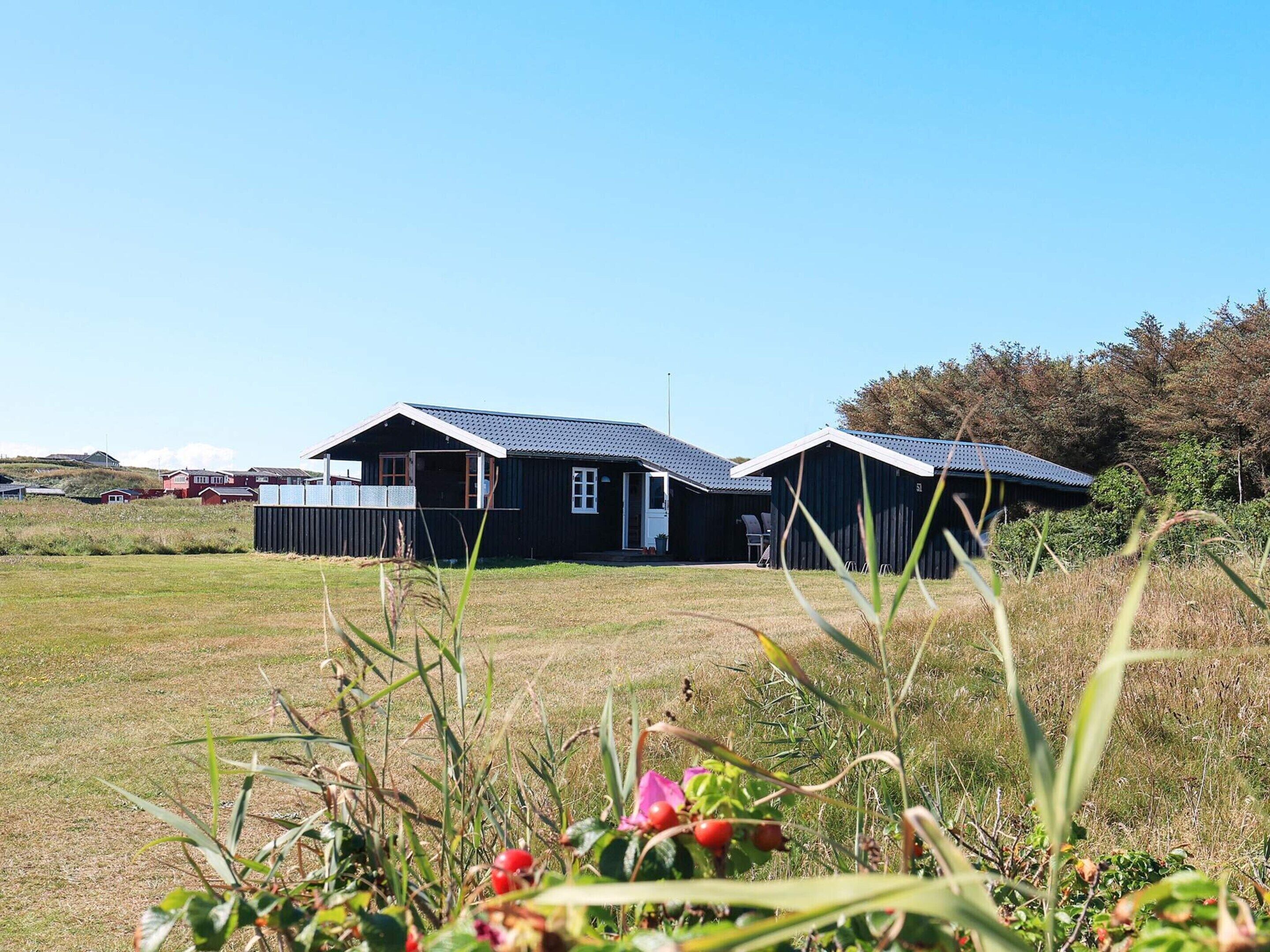 A black building with a sloped roof, surrounded by a grassy field and trees.