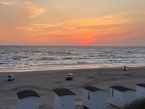 A beach with small white cabins and a sunset over the ocean. - 4 Person Holiday Home in Lokken (Lokken)