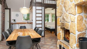 A cozy room with a wooden dining table, chairs, a stone fireplace, a loft bed, and a kitchen area with a ladder.