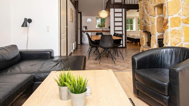 A modern living room with a stone fireplace, leather sofas, and a dining area with a wooden table and chairs.