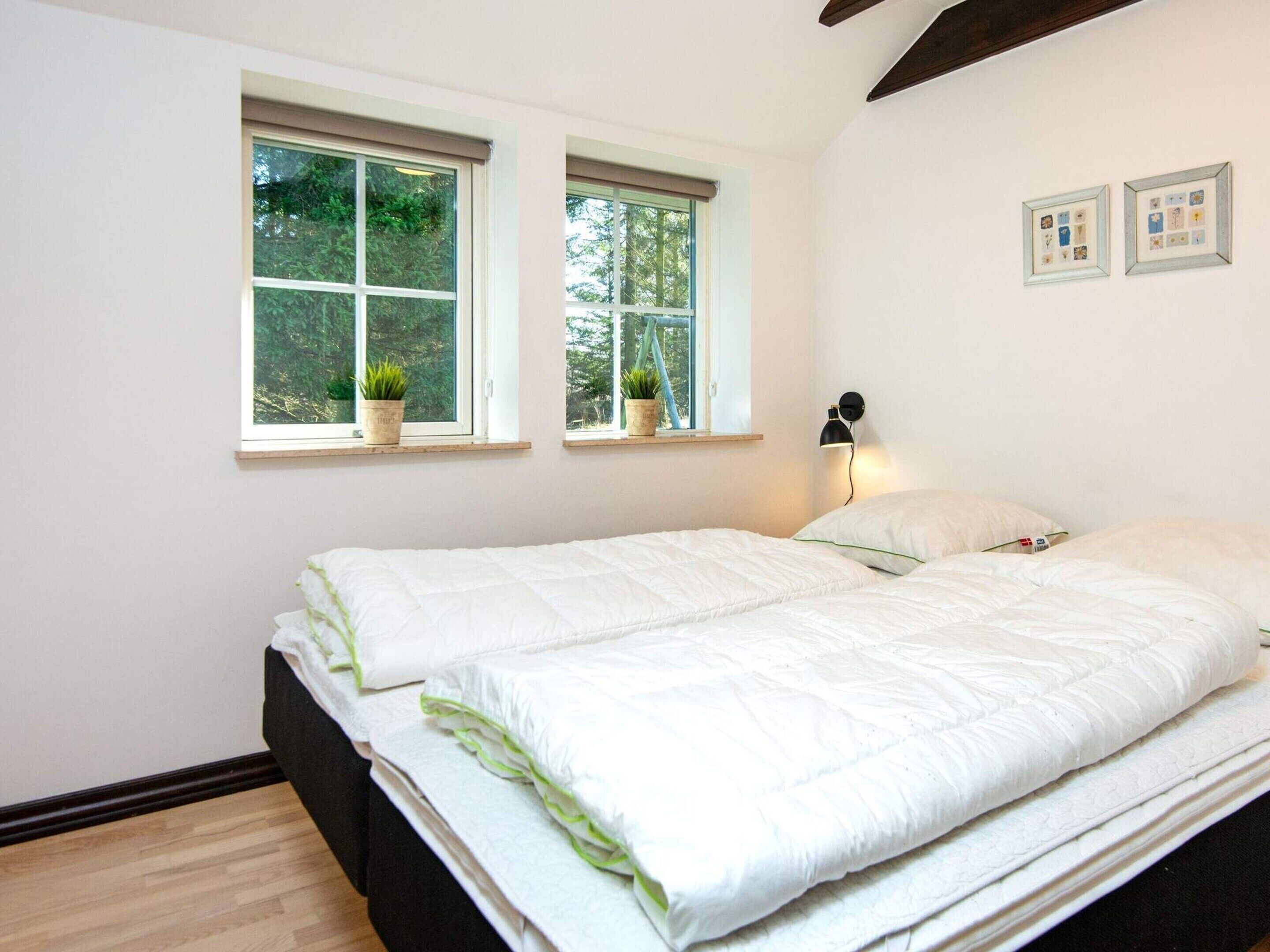 Een slaapkamer met twee bedden, twee ramen met planten, een wandlamp en ingelijste foto's.