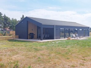 Une maison moderne dotée d’un grand patio, d’un barbecue et d’un espace extérieur aménagé et couvert pour s’asseoir.