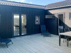 Une terrasse dotée d’une porte-fenêtre coulissante donnant accès à un espace extérieur aménagé avec du mobilier de jardin.