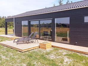 Un edificio moderno con terraza, dos sillones y una puerta de vidrio.