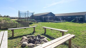 Un espacio al aire libre con césped, mesas de picnic, una fogata y un edificio con techo.