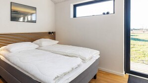 Un dormitorio con una cama, cabecera, ventana y un cuadro en la pared.