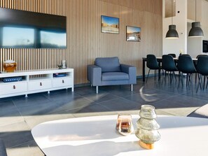 En moderne stue med et fladskærms-tv, en sofa, et spisebord med stole og en dekorativ vase.