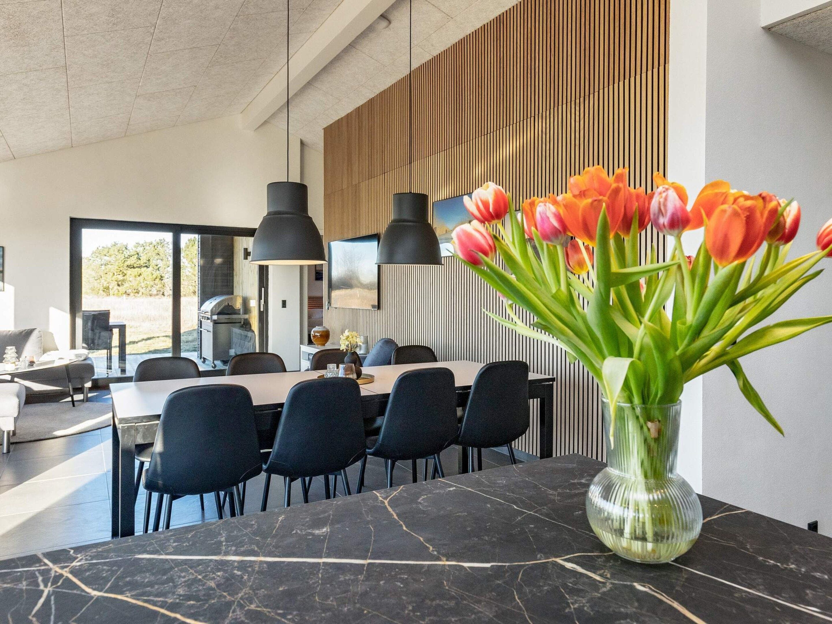 Un espace repas moderne avec une table en marbre, des chaises noires et un vase de tulipes.