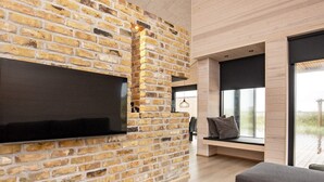 Una sala de estar moderna con pared de ladrillo, un televisor de pantalla plana grande, una mesa de centro redonda y un sofá gris.