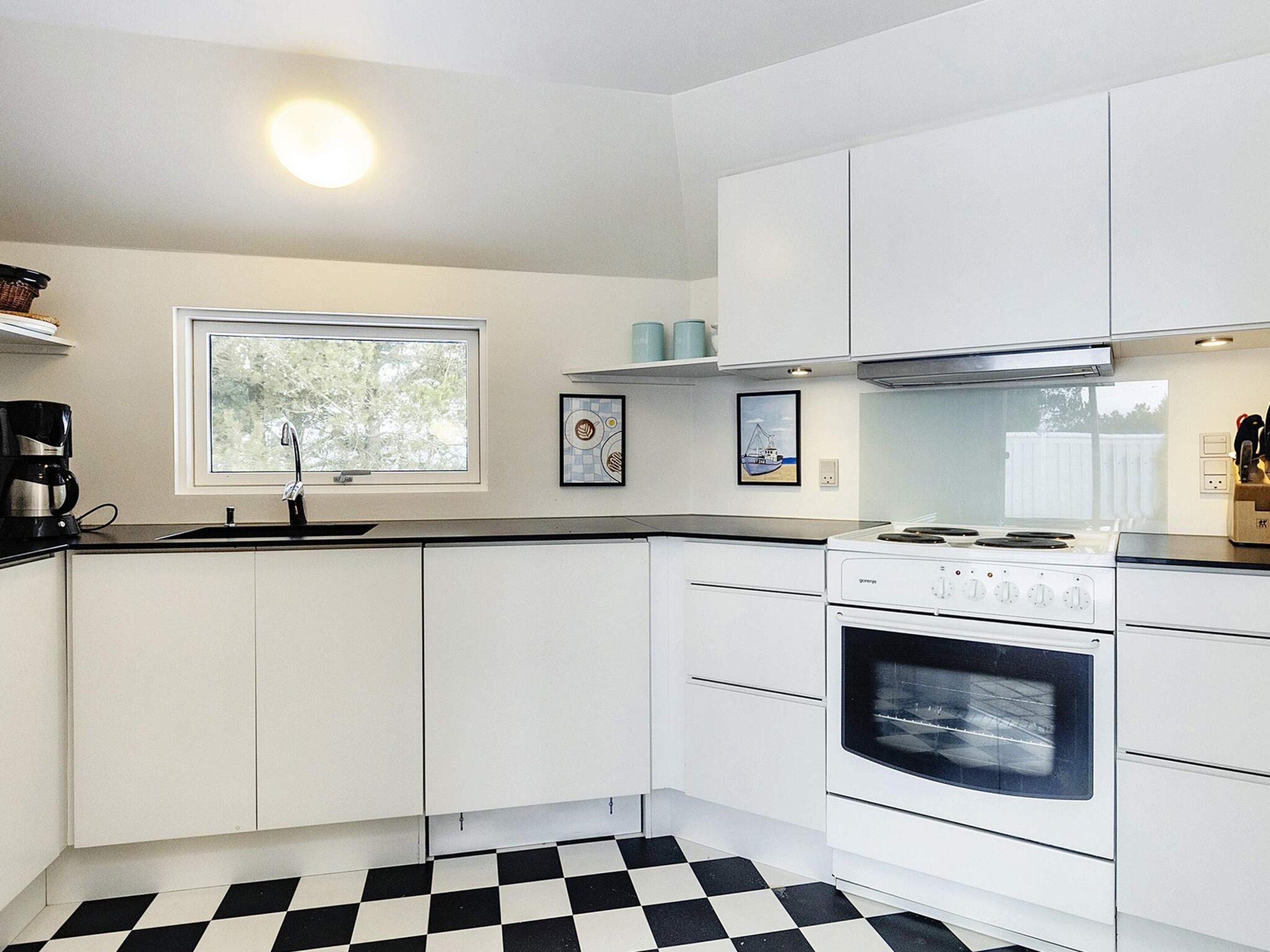 A modern kitchen with white cabinets, a black and white checkered floor, a window, and a stove.