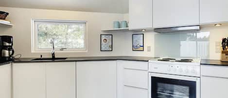 A modern kitchen with white cabinets, a black and white checkered floor, a window, and a stove.